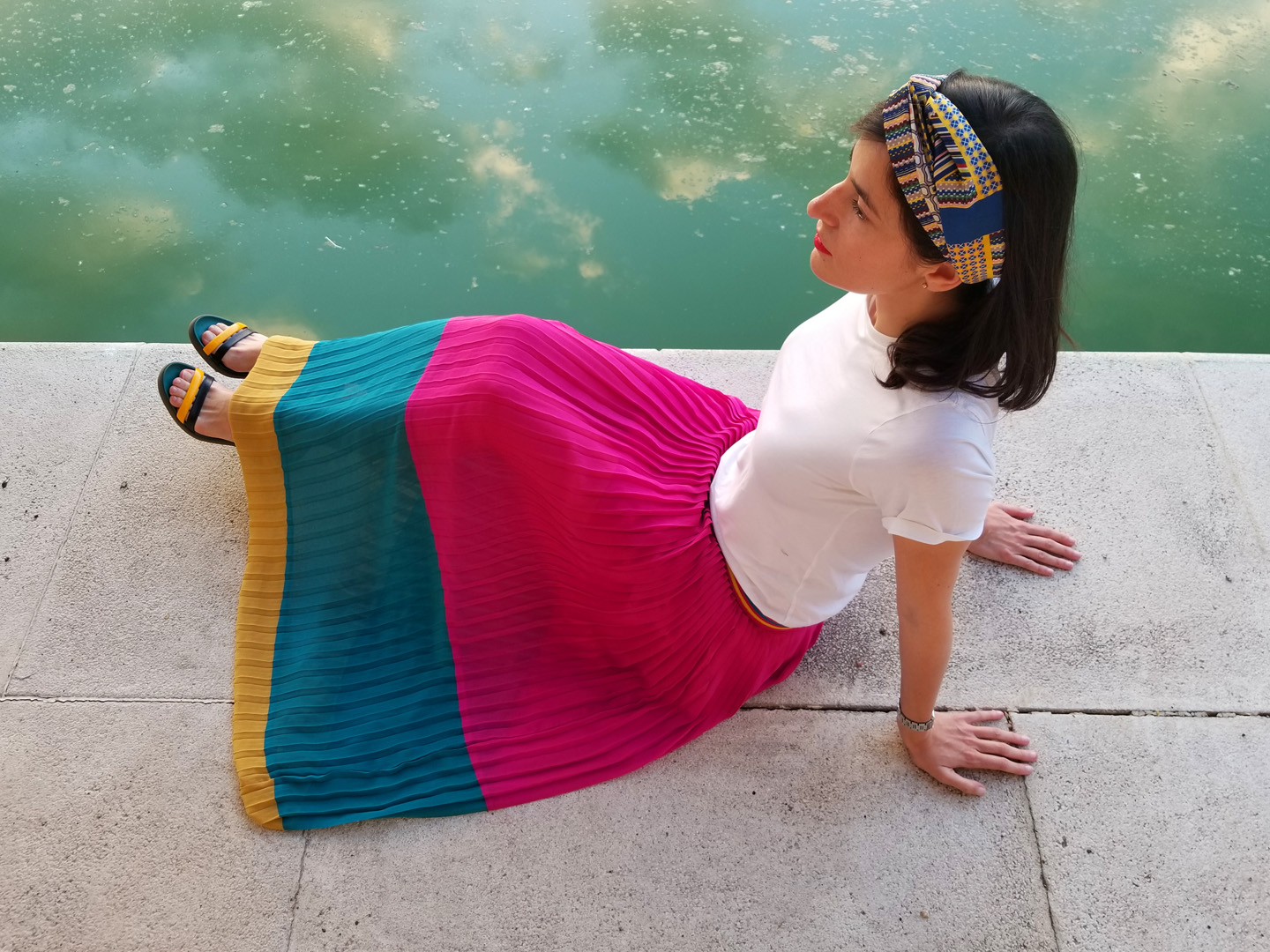Style Indigo wearing a white t-shirt and a pleated skirt by the water